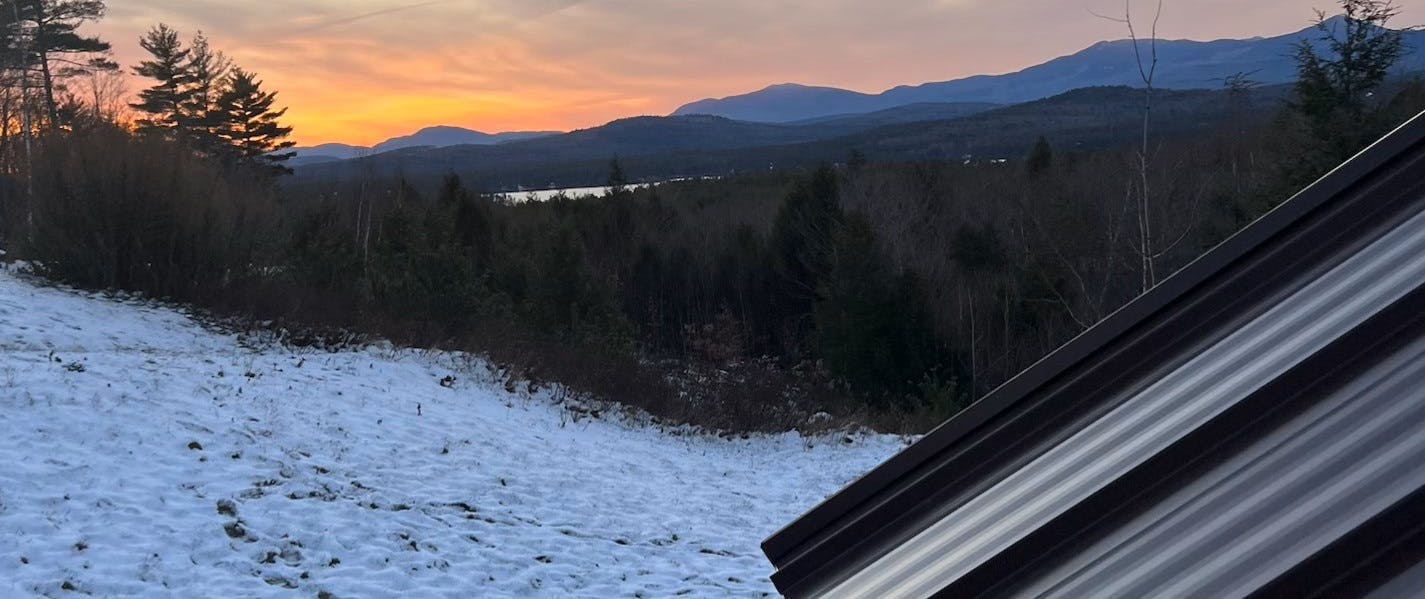 A sunset over the white mountains with a glimpse of metal roof