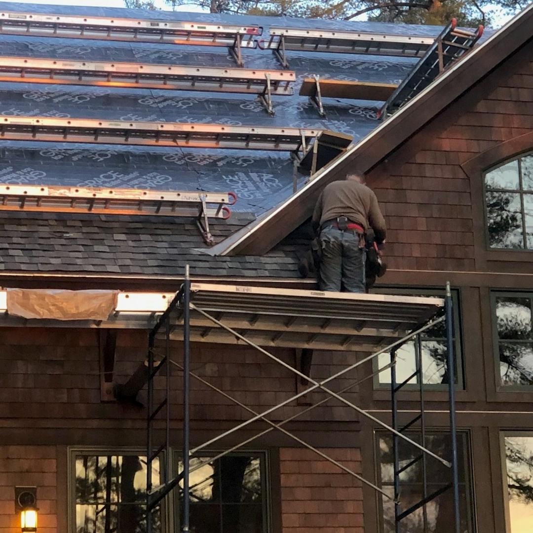 A man working to replace a large shingled roof